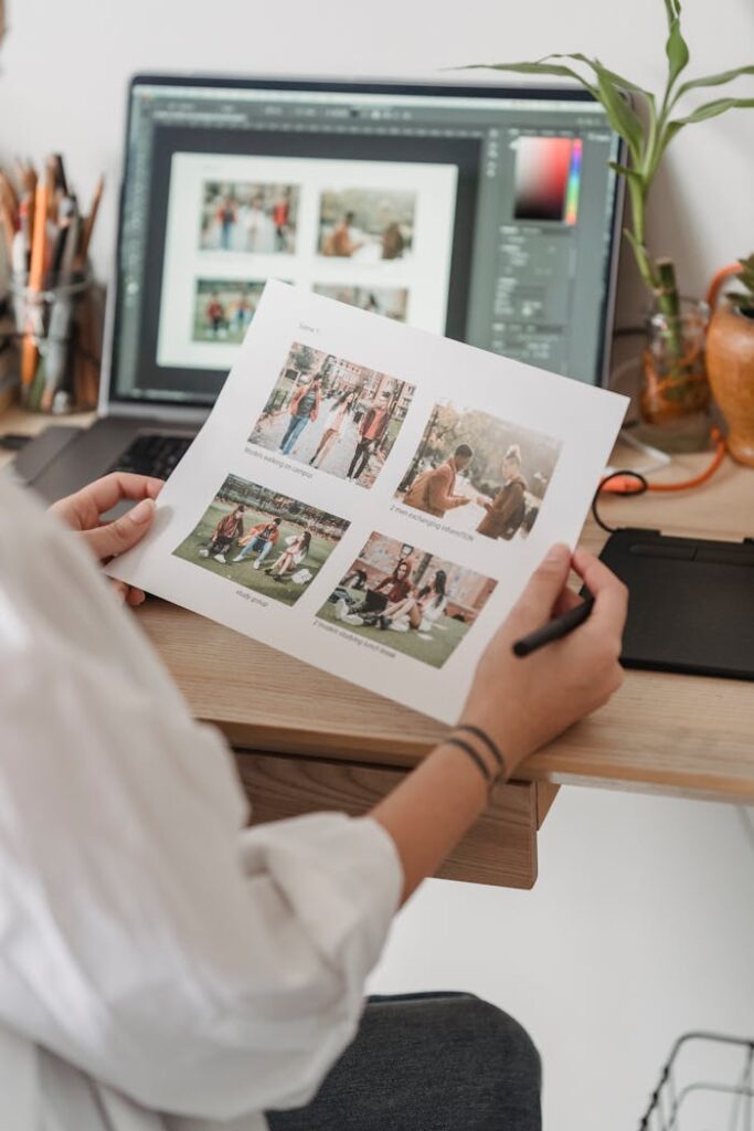 Back view high angle of unrecognizable female photographer sitting at table with netbook and looking through printed photos